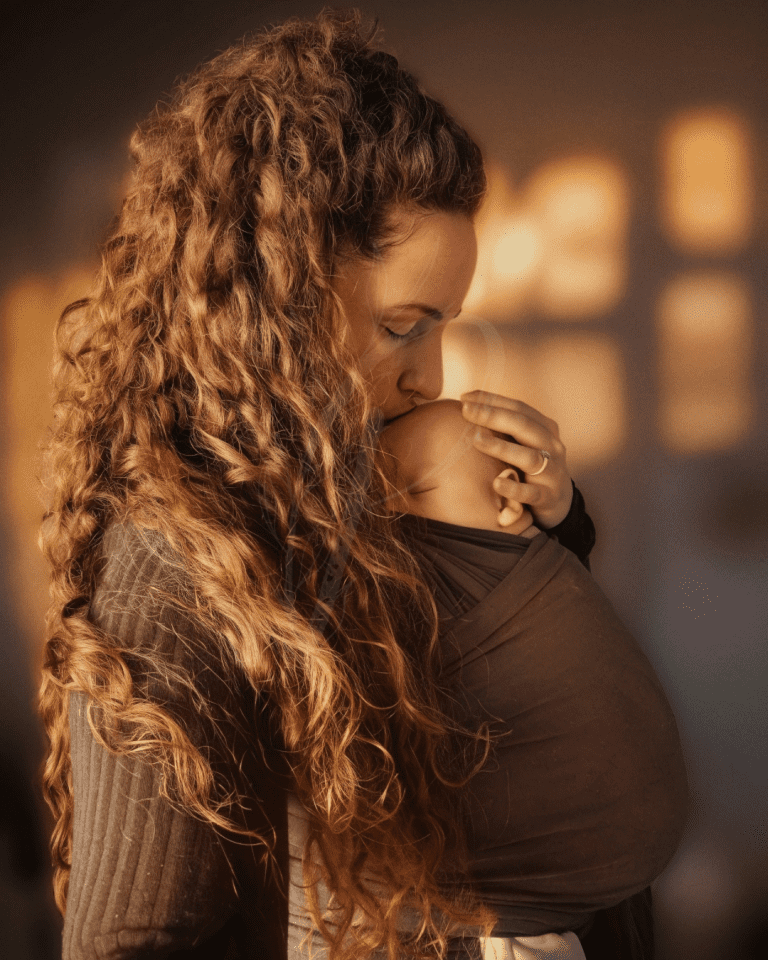 Mother and baby in a sling, mother kissing baby on forehead, baby sleeping