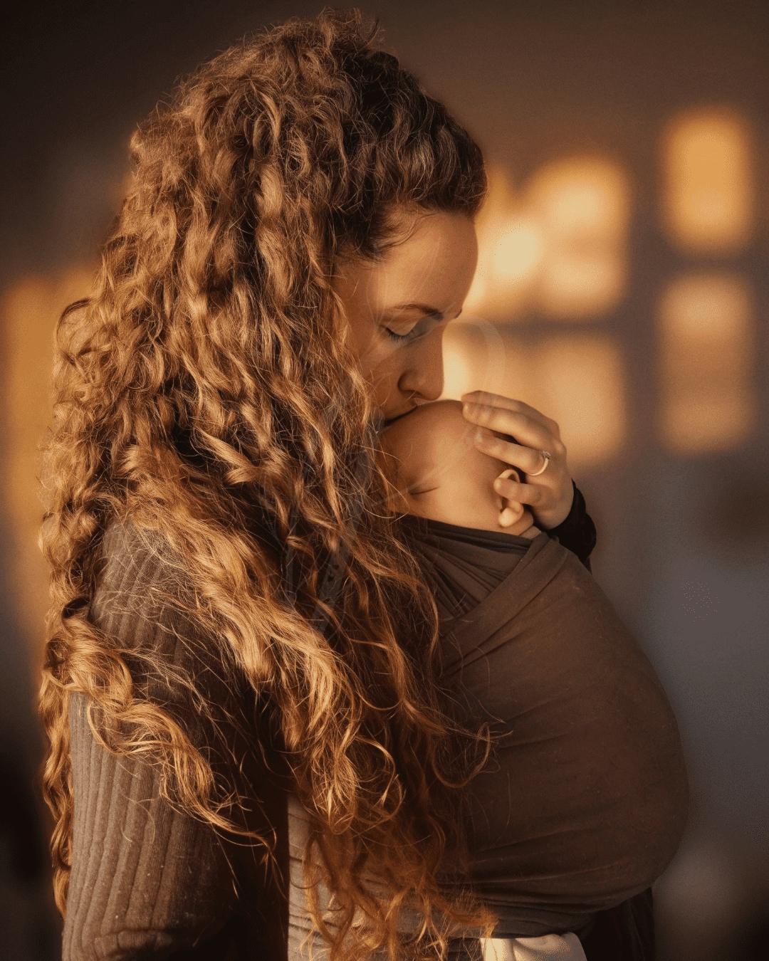 Mother and baby in a sling, mother kissing baby on forehead, baby sleeping