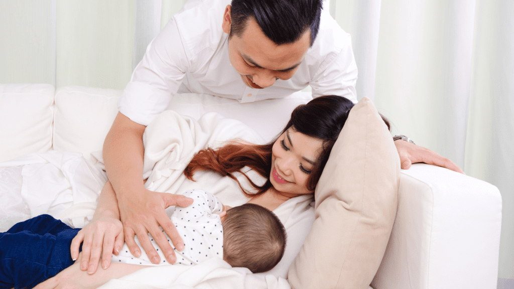 Father supporting new mother breastfeeding on the sofa